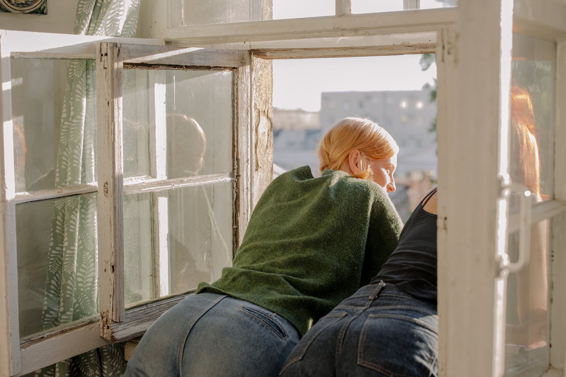 person in green hoodie and blue denim jeans sitting on brown wooden chair